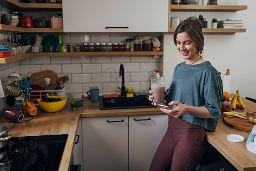 Fit millennial woman drinking milkshake for snack and using smart phone