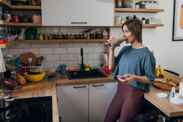 una donna atletica beve un frappè che ha preparato in cucina e naviga in internet - smoothie drinking women drink foto e immagini stock