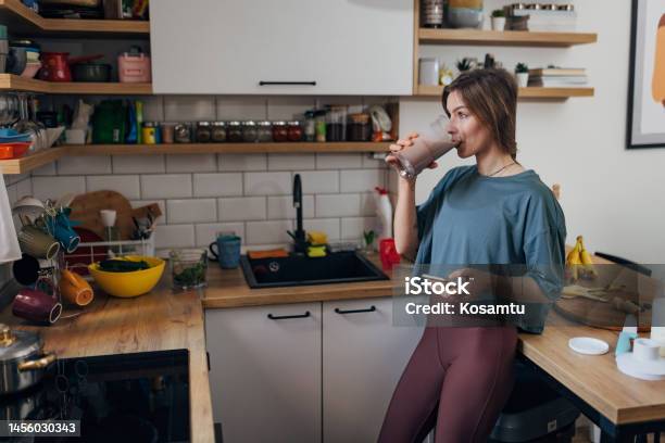 An Athletic Woman Drinks A Milkshake She Made In The Kitchen And Surfs The Internet Stock Photo - Download Image Now