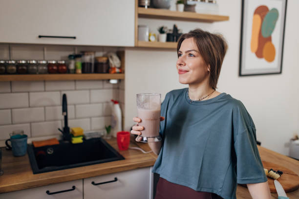 istock Beautiful fit woman drinking milkshake while standing in kitchen 1456030354