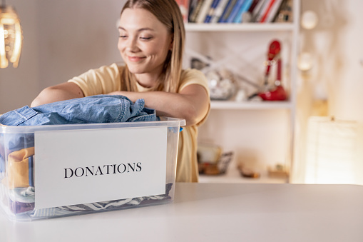 Shot of a smiling young woman ready to donate a full box of clothes to a charity organization