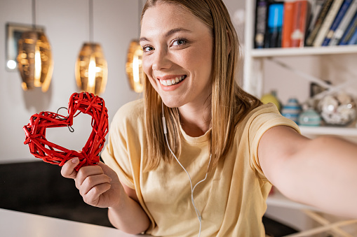 Smiling young woman taking selfie while holding a heart shaped object