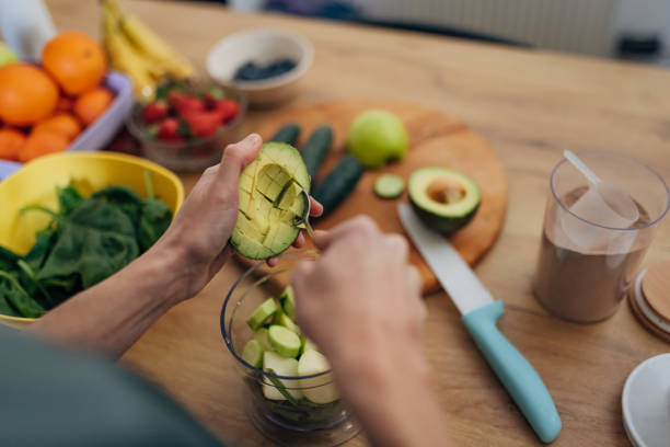 eine nicht erkennbare frau nimmt das fruchtfleisch von einer avocado mit einem löffel in der küche - juicer food and drink healthy eating sport stock-fotos und bilder