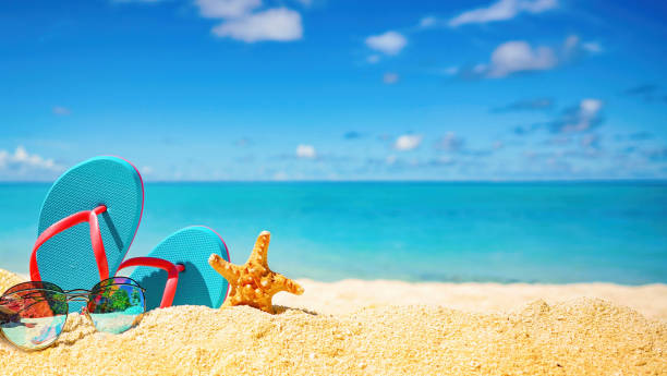 Original beautiful background image on the theme of summer holidays by the sea, with space for text. Beautiful colorful background for summer beach holiday. Sunglasses, starfish, turquoise flip-flops on sandy tropical beach against blue sky with clouds on bright sunny day. starfish sunglasses stock pictures, royalty-free photos & images