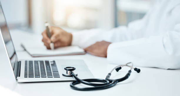 Laptop, stethoscope and doctor writing in notebook for research planning or medical tech innovation in hospital office. Healthcare medic worker, research strategy book notes and online communication stock photo