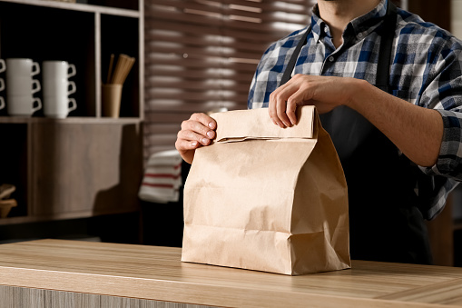 Worker with paper bag at counter in cafe, closeup. Space for text