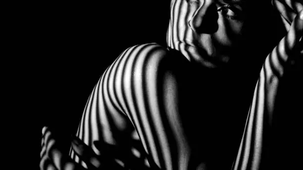 Photo of Female face and body in the shadows of the stripes.  Art shot black and white.