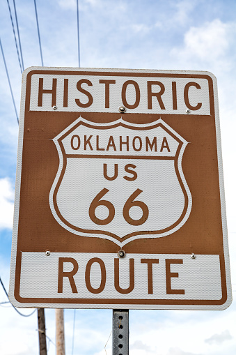 A brown and white road sign of the historic Route 66 against blue sky.