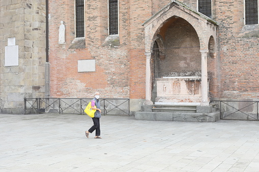 Historic center of Padua during the Covid 19 pandemic. Woman wears a surgical mask a she walks alone in the Saint Square (Piazza del Santo). In the background the Basilica of St. Anthony of Padua.