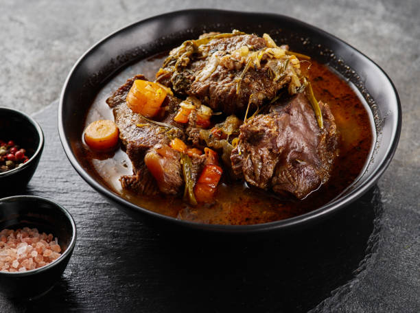 Traditional German braised beef cheeks in brown red wine sauce with herbs as closeup in black plate. Traditional German braised beef cheeks in brown red wine sauce with herbs as closeup in black plate cheek stock pictures, royalty-free photos & images