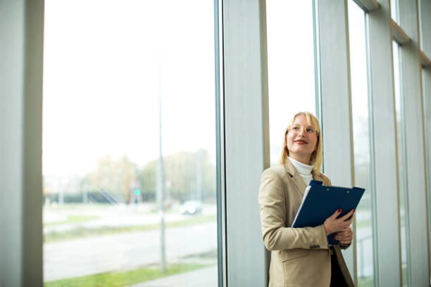 istock Beautiful blond female holding file folder at the office corridor 1456048883