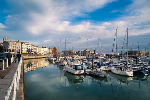 Ramsgate, UK - Dec 20 2022. Ramsgate harbour on a bright winter day with white clouds reflecting in the marina along with the reflections of the waterside buildings.