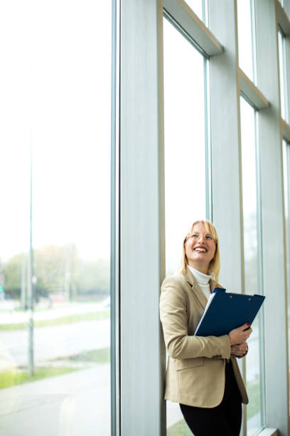istock Beautiful blond female holding file folder at the office corridor 1456049674