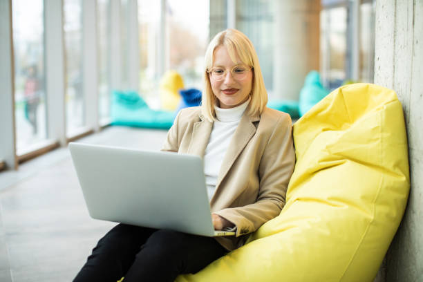 Female student typing on a laptop Cheerful Caucasian woman, sitting on the steps, smiling and using her laptop while typing something on a computer. beanbag stock pictures, royalty-free photos & images