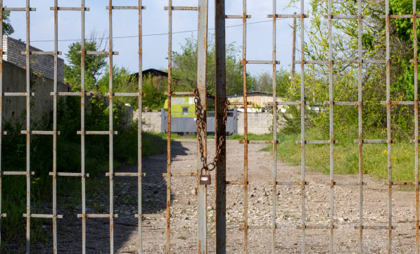 istock Old rusty iron gate on chain and lock. Closed metal gates. Protection, security and safety concept. padlock on metal gate closeup 1456050084