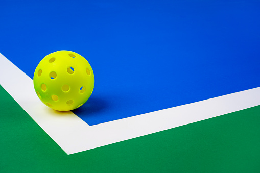 Outdoor Pickleball on the court line. Yellow Pickleball with Blue interior, white line and green exterior..