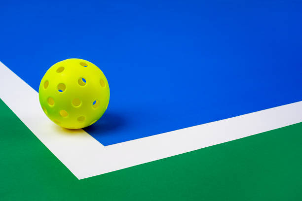 Outdoor Pickleball on the court line Outdoor Pickleball on the court line. Yellow Pickleball with Blue interior, white line and green exterior.. pickleball equipment stock pictures, royalty-free photos & images