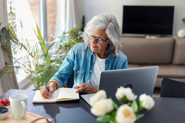 istock Beautiful senior woman working with laptop while checking some documents in the kitchen at home. 1456054474