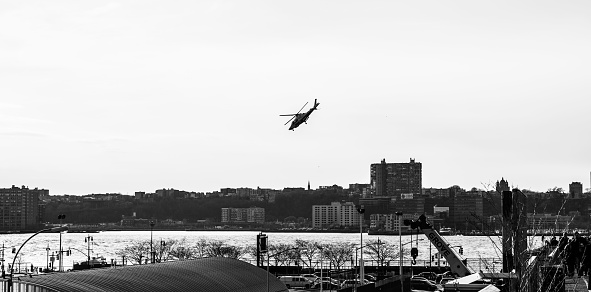 A grayscale shot of a helicopter over an urban scenery in New York with the Hudson River in the background