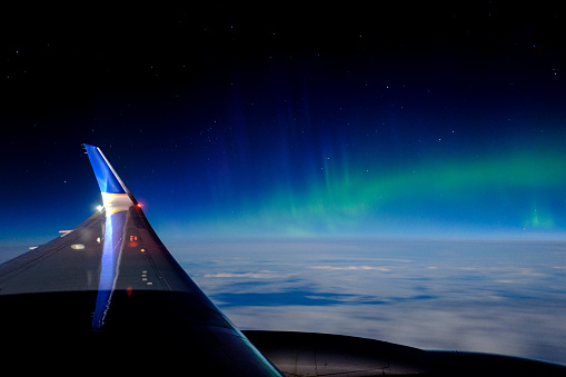 During a night flight from Chicago to London, the Northern Lights (aurora borealis) are visible over the North Atlantic with the earth below and stars above.