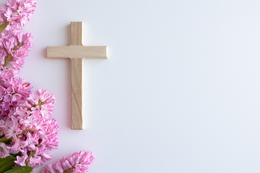 Simple wood Christian cross on a white background with border of pink hyacinth flowers with copy space shot from above