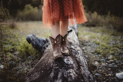 Child walking across a log with a dress and boots