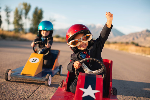 Two young boys dressed in business suits are racing in toy cars and competing against each other to better their business resumes. Image taken in Utah, USA.