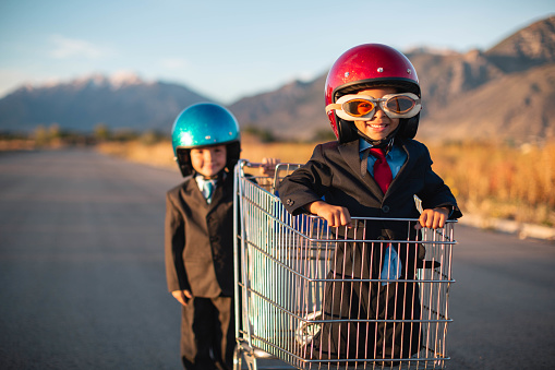 Two young boys dressed in business suits are racing in a shopping cart and competing against each other to better their business sales. Image taken in Utah, USA.