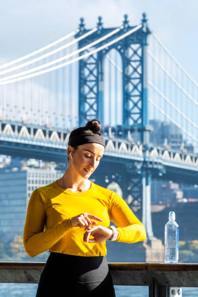 портрет подтянутой женщины, наслаждающейся активным днем в нью-йорке и имеющей манхэттенский мост в качестве фона - east river audio стоковые фото и изображения