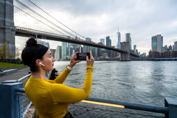 женщина отдыхала после занятий фитнесом и фотографировала манхэттен на телефон - east river audio стоковые фото и изображения