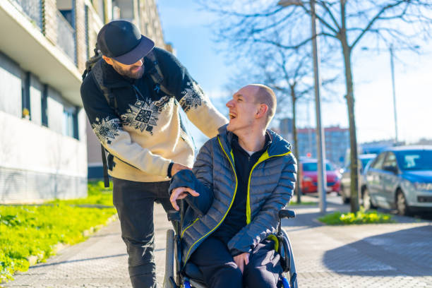 A disabled person in a wheelchair with a friend smiling, handicapped normality A disabled person in a wheelchair with a friend smiling, handicapped normality disabled sign stock pictures, royalty-free photos & images