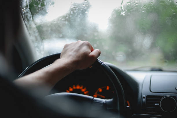 istock Young caucasian guy keeps his hand on the steering wheel while driving a car on a rainy day 1456065100