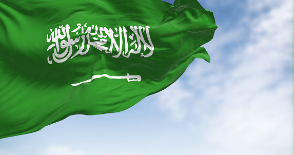 Saudi Arabia national flag waving in the wind on a clear day. Green field with Shahada and sword in Thuluth script. Rippled fabric. Realistic 3d illustration