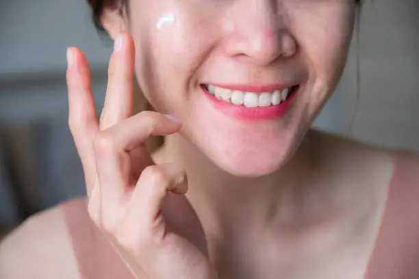 Photo of Cropped shot of Asian woman applying cream on her face for treating redness skin.