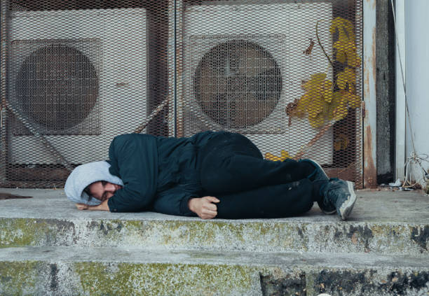 istock Frozen homeless man sleeps on concrete near building's ventilation system. Problem of how homeless survive winter cold 1456078191