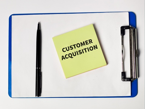 Customer Acquisition written on sticky note with a pen and paper board.