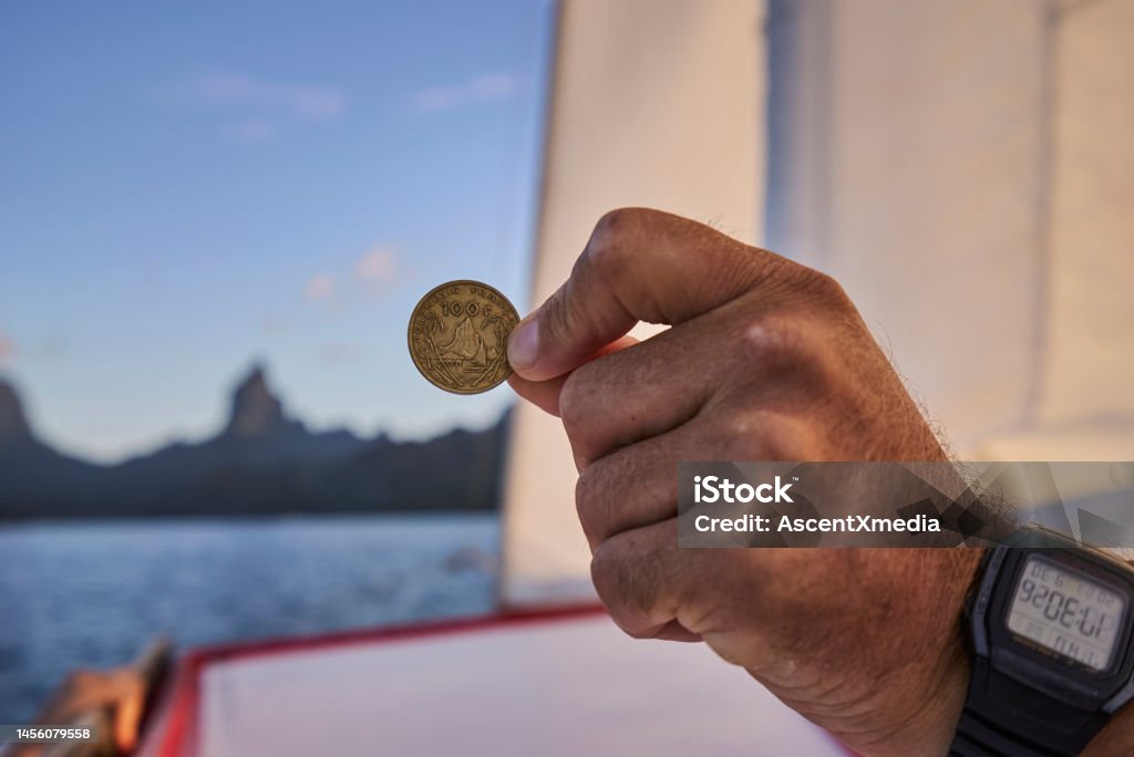 Hand with digital watch holds old coin on boat Tropical lagoon and mountains behind Adult Stock Photo