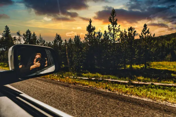 Photo of Woman on a road trip takes a photo with a camera out of a car window reflected in side mirrors of stunning natural landscape