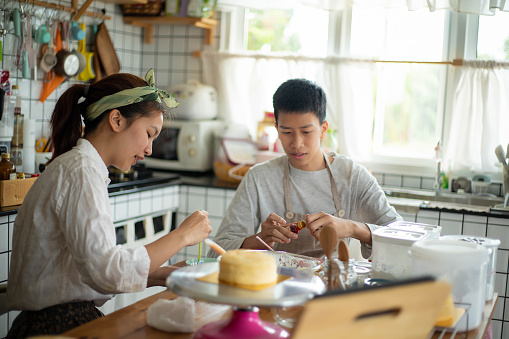 Teenage girl and boyfriend decorating sweets in the kitchen at home.