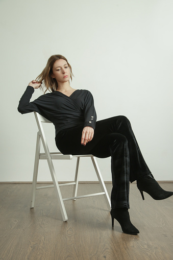 Studio photo of young female model wearing all black outfit, long sleeve cotton shirt, black plush trousers and high heels