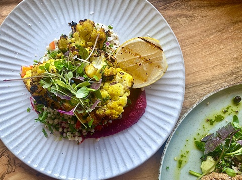 Horizontal flatlay lunch of grilled + moroccan spiced caulliflower with beetroot paste, couscous salad + micro greens on ceramic plate on wood table resturant near Coffs Harbour NSW Australia