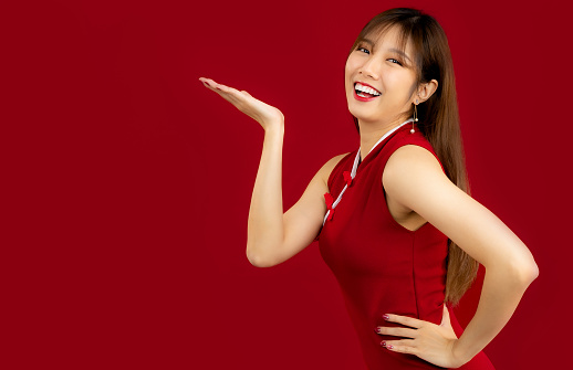 Young beautiful asian woman long hair style smiling and hand pointing free space red background. Happy Chinese New Year.