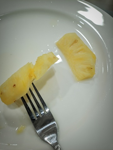 two pieces of pineapple on a plate with a fork, at breakfast