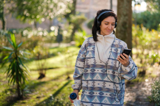 istock Woman walking in the park while looking at her cell phone 1456103317
