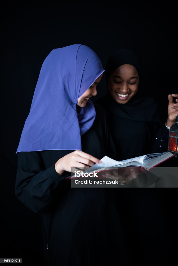 Muslim women reading kuran to ramadan Two young woman muslims standing reads a koran at home Adult Stock Photo