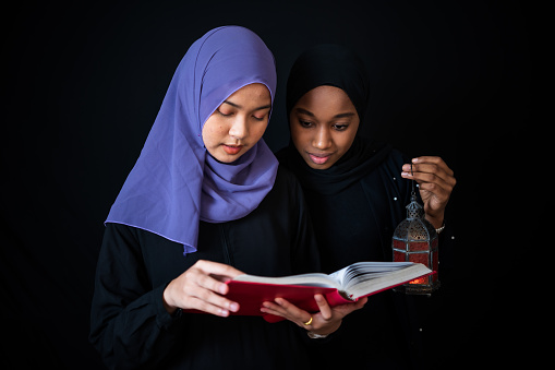 Two young woman muslims standing reads a koran at home