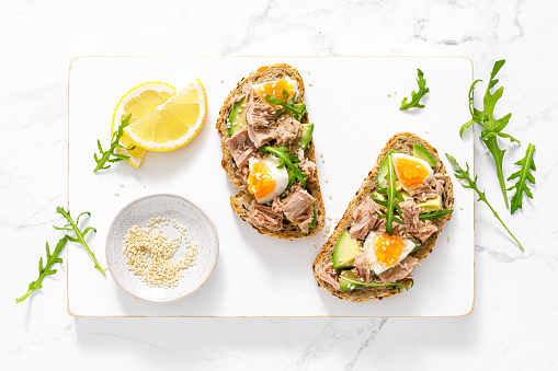 Tuna toast. Open sandwiches with whole grain bread, canned tuna, boiled egg, avocado and arugula. Top view