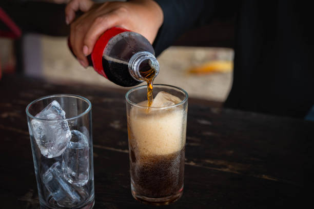 Woman holding pouring cold cola soft drink soda, sparkling water with ice sweet sugar from bottle into glass in her hand. Health care, healthy diet lifestyle concept. Woman holding pouring cold cola soft drink soda, sparkling water with ice sweet sugar from bottle into glass in her hand. Health care, healthy diet lifestyle concept. coca cola stock pictures, royalty-free photos & images