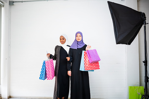 Portrait of two muslim women holding bags and laughing on white background