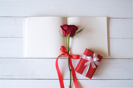 Blank notebook with red roses and red gift box on wooden table. Copy space for your text. Valentine's day, wedding, birthday and special occasion concept. Copy space for text. Top view, Flat lay.